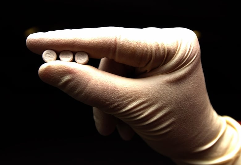 A gloved hand holds three white pills.