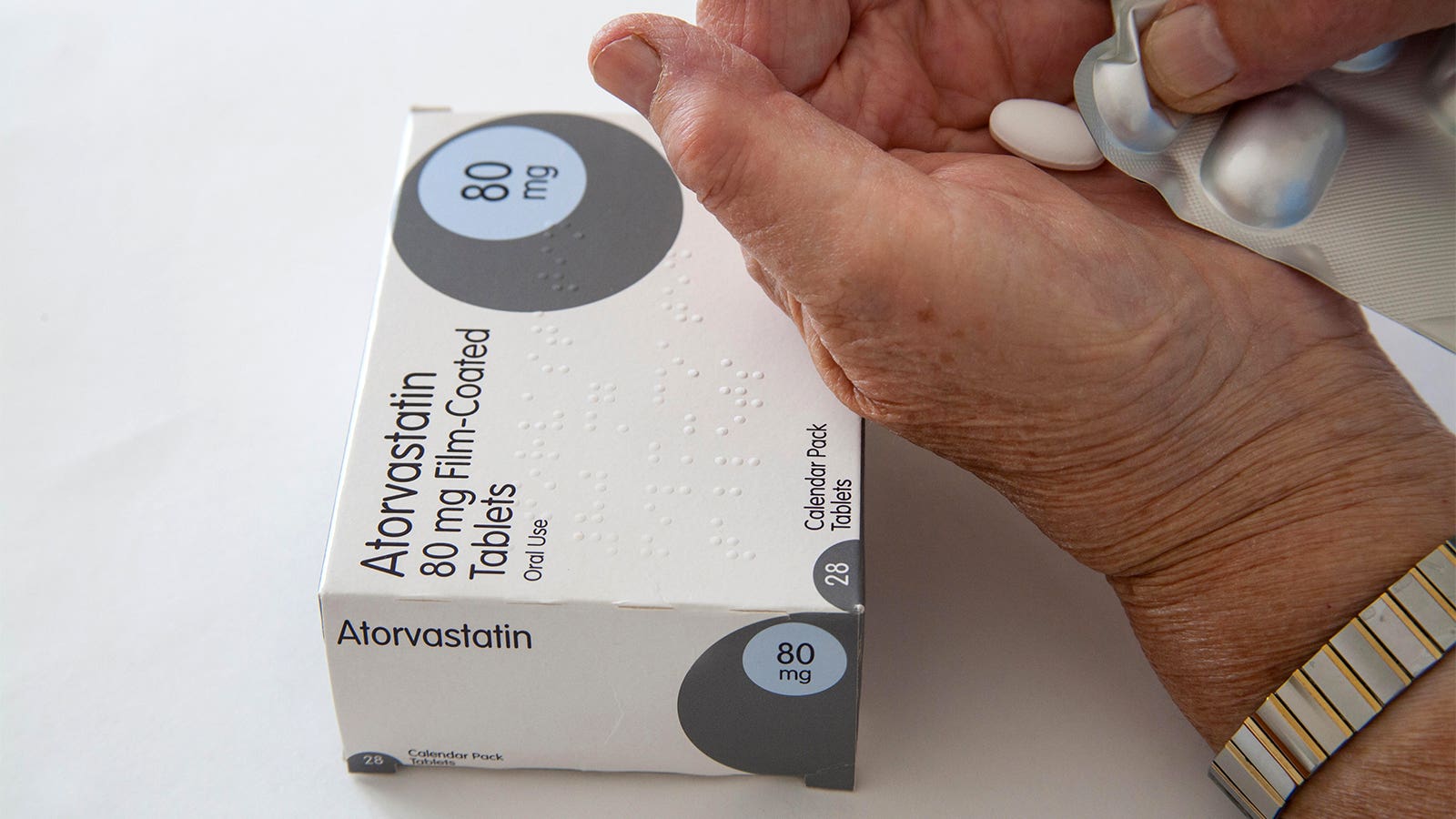 A photo of a woman pushing an atorvastatin tablet from its blisterpack.