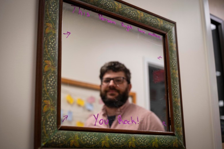 A man with a beard stands in front of a mirror.